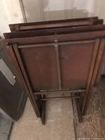 Side view of four vintage wood and metal TV trays stacked folded against wall.