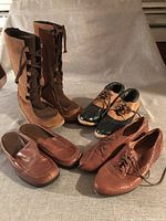 Four pairs of women's shoes and boots including tall lace-up boots, duck shoes, slip-ons, and oxfords arranged on a neutral fabric background.