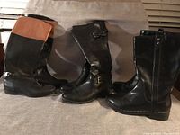 Three pairs of women's mid-calf boots arranged side by side on a fabric background. Each pair features different design details like buckles, buttons, and colored cuffs.