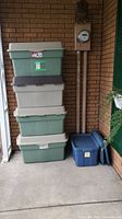 Stack of four Rubbermaid storage bins: three green with beige lids and one beige with brown lid, stacked vertically.