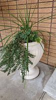 White cement planter urn with artificial plants shown from front next to brick wall and green door.