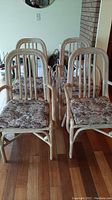 Group front view of four rattan chairs with floral seat pads on hardwood floor