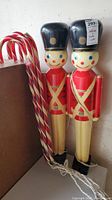 Two vintage blow mold soldier figures standing upright with four candy cane decorations beside them.