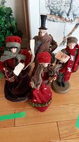 Overview of four caroler figurines on wooden floor
