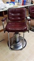 Front view of the red vinyl hair salon chair showing padded seat and backrest, chrome armrests, and circular base.