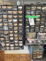 Front view of three large plastic storage units and one smaller metal storage organizer containing assortments of hardware items such as screws, nuts, bolts, and hooks.