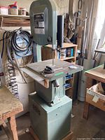 Front view of bandsaw showing table, blade, and pedestal base on wooden platform