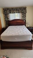 Front view of queen bed with mattress and headboard, showing wood finish and mattress condition.