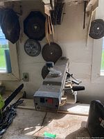 Side view of radial arm saw showing the motor, adjustment ruler, and attached handles. Several circular saw blades visible behind on the wall.