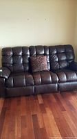 Front view of brown leather sofa, three tufted back cushions and a decorative brown patterned pillow on center seat.