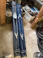 Two blue metal folding saw horses folded and placed on floor showing their compact form and locking mechanism.