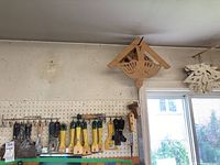Photo shows scrapers and putty knives hanging on pegboard, various sizes and handle types visible.