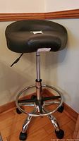 Photo of the stool showing black vinyl seat with curved backrest and cutout, chrome frame, and caster wheels.