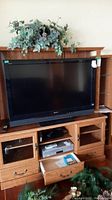 Sony Bravia television displayed on wooden entertainment unit, shows full front view of TV screen and part of stand and shelves below with remote placed on top.