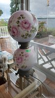 Full view of vintage painted glass double globe hurricane lamp showing pink rose floral patterns on upper and lower globes, metal base, and glass chimney.