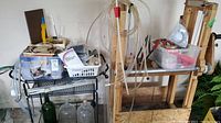 Overview photo showing wine making equipment organized on metal racks and wooden press rack with hoses and accessories poised on top and hung around them.