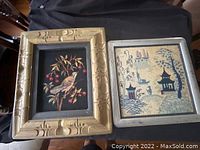 Two antique picture frames displayed side by side on a black surface showing the front embroidered artwork.