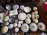 Full overview of the lot showing multiple antique plates, serving pieces, a vase, and glassware on a black background