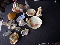 Top-down view showing the collection of porcelain figurines, ceramic lamp, cookie jar, religious statues, and decorative trays arranged on a black tablecloth.