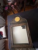 Front view of the antique wood clock with round clock face on top and mirror below, sitting on a black surface.