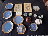 Full lot overview showing 6 blue plates with gold rims, framed artwork and small vases.