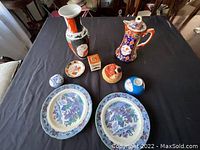 Overview of all items on black cloth background including two plates, two pitchers/vases, and four small decorative figurines or containers