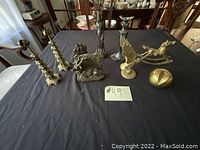 Photo showing the complete assortment of seven brass items arranged on a black cloth including candle holders, animal statues, and decorative pieces.