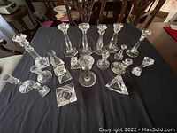 Wide view of 19 clear crystal candle holders in various sizes and shapes on black cloth