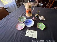Full view of porcelain tea pot, four decorative plates with distinct floral and landscape designs, two small enamel vases, and small sugar bowl on black cloth surface.