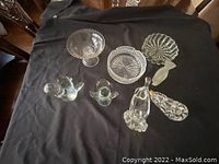 Lot of clear glass items on black cloth including figurines, candy dishes, and ashtrays.