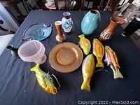 Overview of various glass and ceramic decorative items, including fish-shaped figurines, multiple vases, a dish, and plates on a table
