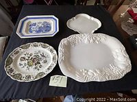 Four platters displayed on black cloth: white and blue rectangular, white with floral, white with grapevine embossing, white scalloped.