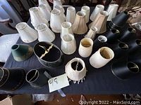 Top view of various mini and medium lamp shades including black metal and white fabric shades on a dark tablecloth.