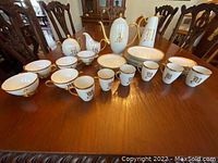 Front view of full china set on wood table showing teapot, coffee pot, cups, saucers, sugar, creamer, and plates.