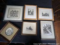 Six antique framed pictures displayed on a table, varying styles of frames and black and white architectural prints