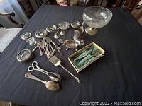 Overall lot items on table including silver ashtrays, forks, tongs, serving spoon, and large fruit bowl