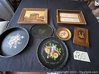 Photo showing seven items: two large round tin trays with floral designs, one smaller black metal tray, two rectangular wood frames, one small wooden art piece, and one small broken wood item.