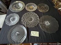 Top-down image of seven crystal platters including three identified as Val St Lambert and Hisey, showing detailed patterns and sizes.