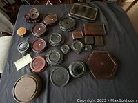 Photo showing all wood stands laid out on black fabric surface, displaying variety in shapes and sizes including round, oval, hexagonal, rectangular, and carved styles.