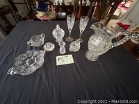 Wide view of entire lot on black cloth showing all glass and crystal items including two wine glasses, pitcher, candy dish with lid, creamer, sugar bowl, and small tray.