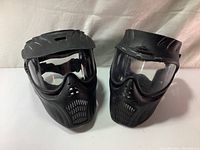 Two black Extreme Rage paintball masks with clear lenses viewed frontally showing the protective face area and ventilation design