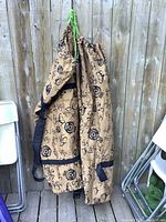 Two large brown camouflage duffle bags hanging on a wooden fence, showing size and camouflage print with black straps and green drawstring.