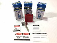 Three red nylon Brady padlocks with aluminum shackles, accompanied by keys and various lockout safety labels in multiple languages.