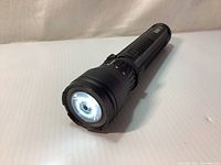 Front angle shot of flashlight head showing lit LED and lens.