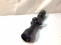 Side angle view of matte black scope showing adjustment turrets and red accent ring near objective lens