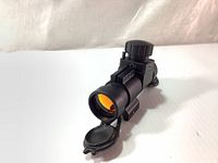 Full view of the Millett red dot sight showing front end with flip-up lens cover open, amber coated objective lens, and side mounting rail.