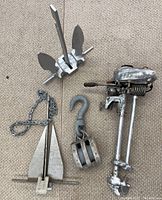 Overhead view showing two metal anchors, metal pulley block with hook, and outboard kicker motor, all used and untested.