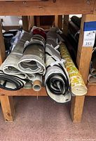 Photo showing multiple fabric rolls of canvas, vinyl, and printed upholstery fabrics stacked on wooden shelving.