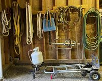 Full view of hanging livestock ropes, propane tank on stand, and metal hand truck dolly