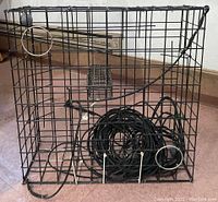 Showing front side of wire crab pot with circular entry rings and coiled black rope line inside, with gray spherical weights attached.